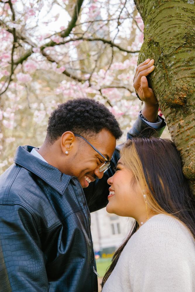Couple laughing forehead to forehead under cherry blossom