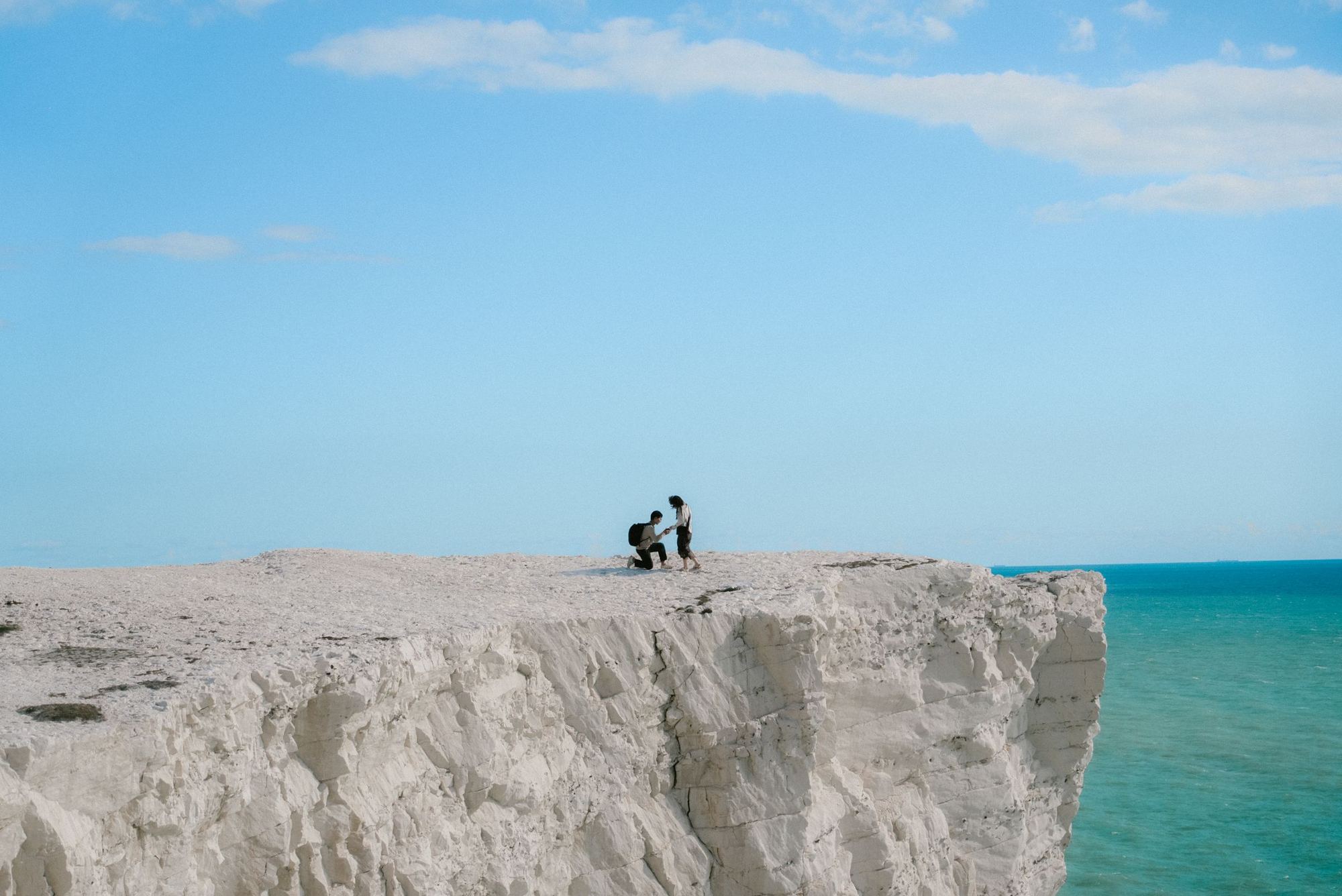 A tiny couple proposing on the edge of the white Seven Sisters cliffs