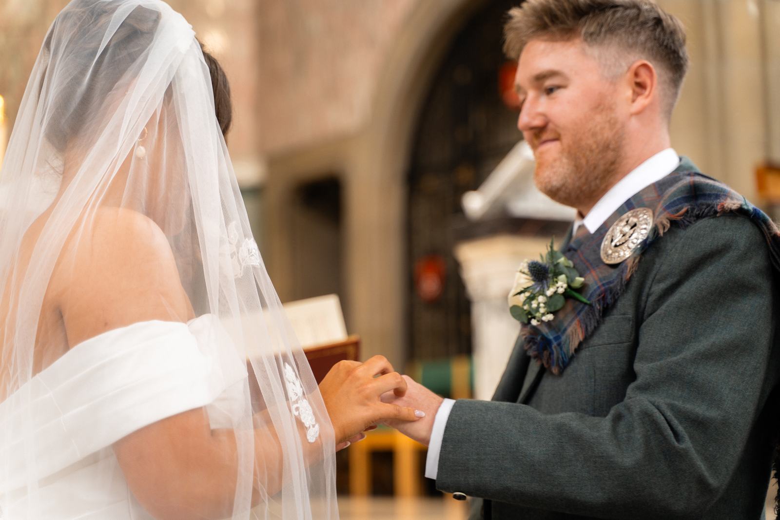 Groom grinning as he places the ring on the bride