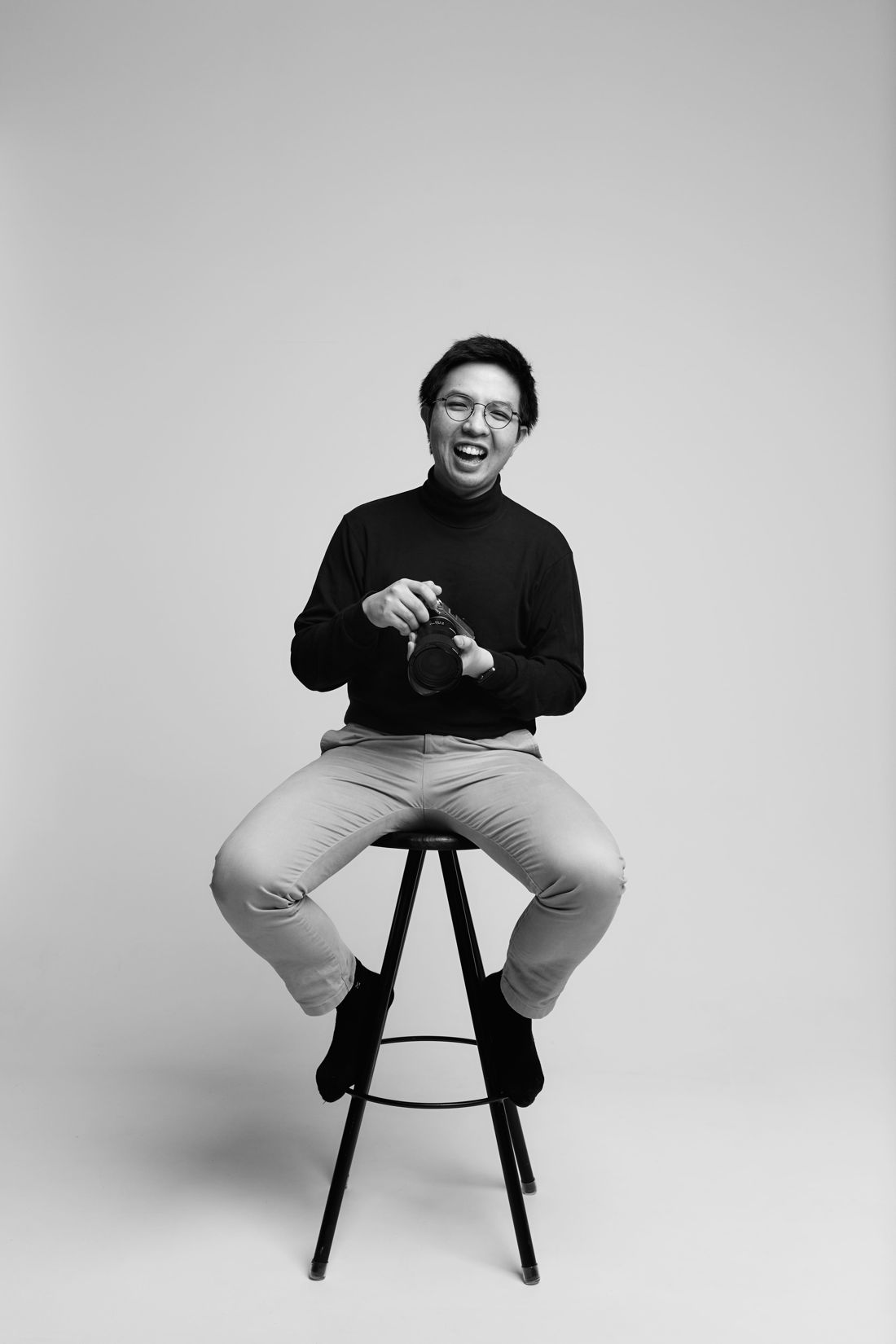 Stefan laughing on a stool, holding his camera
